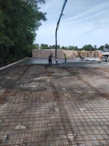 Ouvriers coulant une dalle de béton avec pompe et treillis soudé sur un chantier de construction en extérieur.