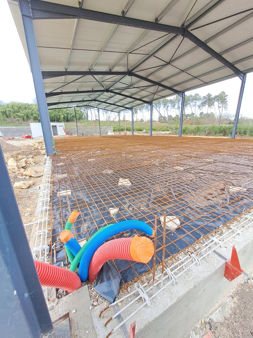 Préparation d'une dalle béton sous hangar métallique avec treillis d'armature, film polyane et gaines techniques.