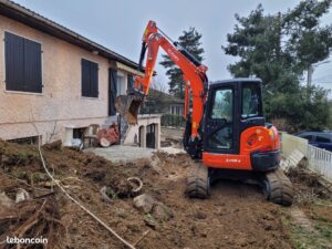 Mini-pelle orange Kubota U48-4 en plein terrassement d'un jardin devant une maison résidentielle.