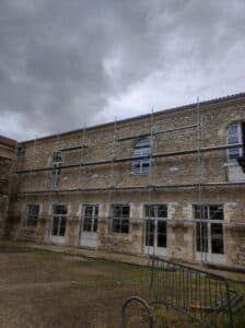 Échafaudage AFIX devant un bâtiment ancien en pierre en rénovation sous un ciel gris couvert.