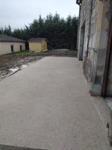 Terrasse en béton désactivé devant une maison en pierre avec un abri de jardin jaune en arrière-plan.