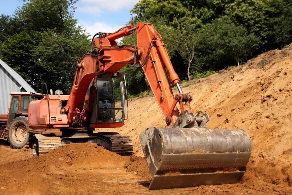 Pelle mécanique orange sur un chantier de terrassement déblayant un talus de terre avec son godet.
